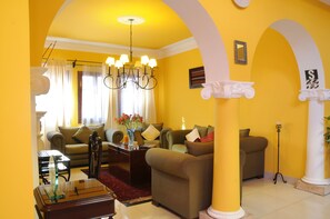 Uma sala de estar com paredes amarelas, um lustre, um sofá e uma mesa de centro.