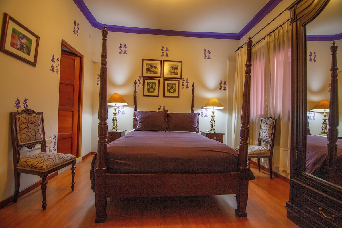 A four-poster bed with a wooden frame, two nightstands with lamps, a chair, and a mirror.