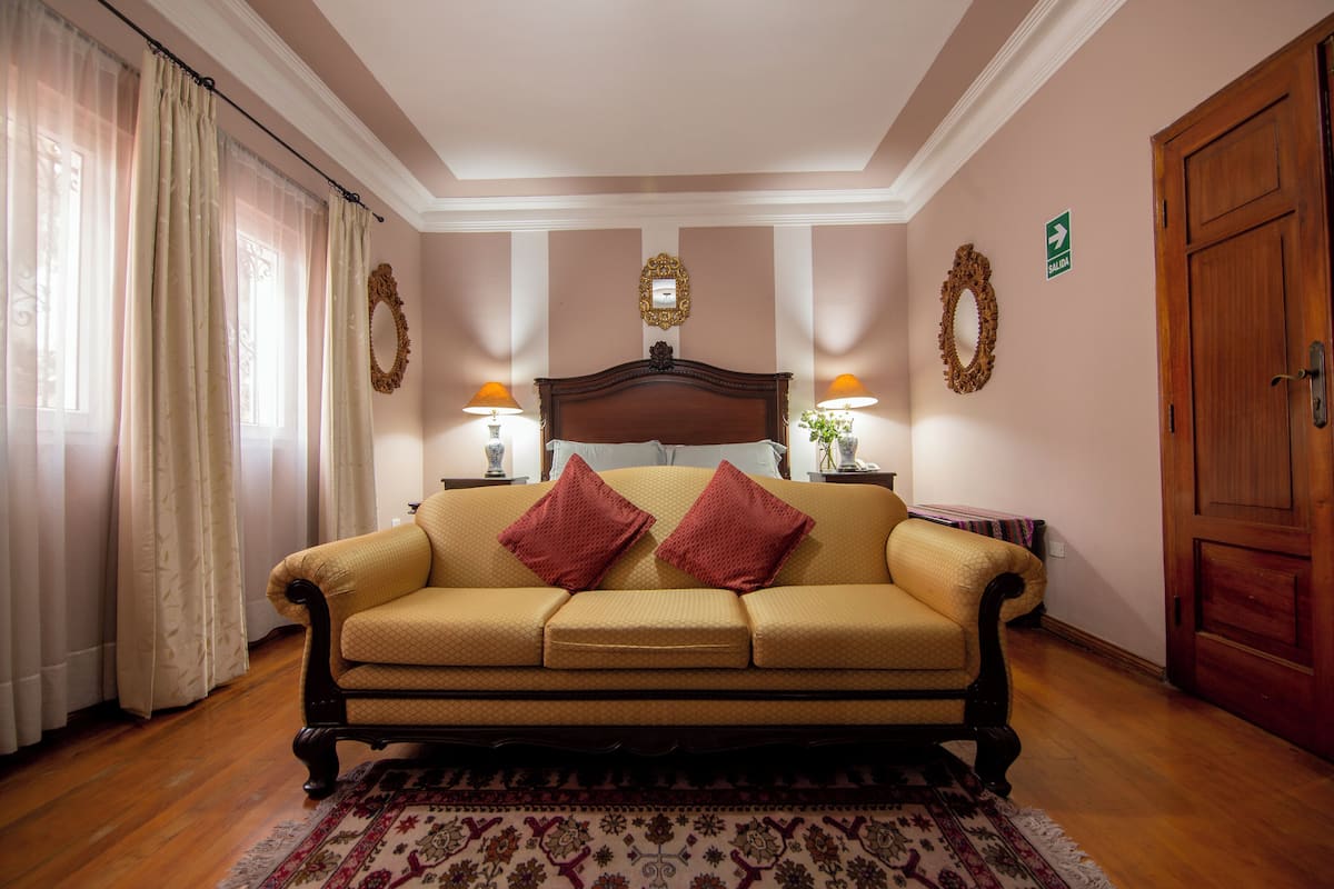A room with a beige sofa, two red pillows, a wooden headboard, and a patterned rug.