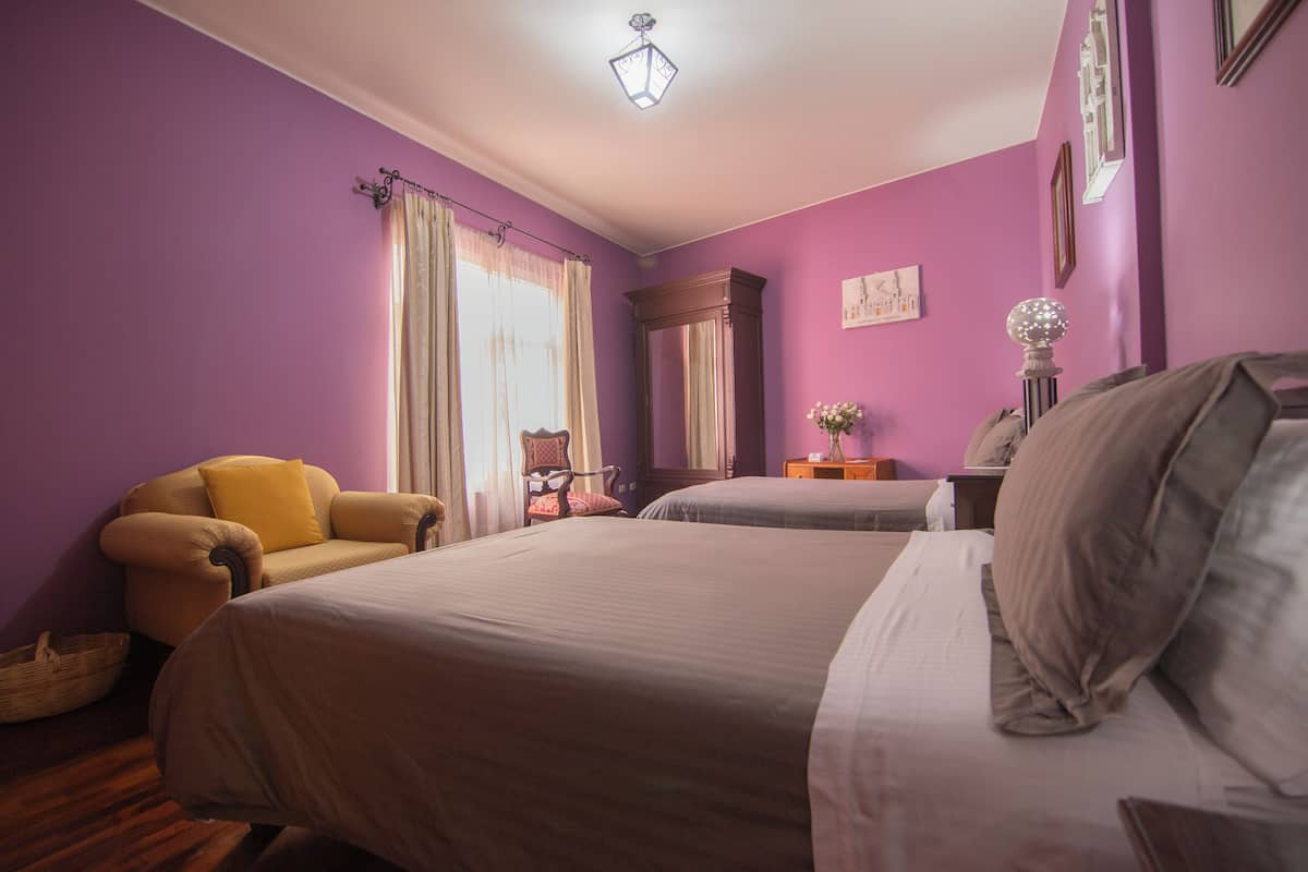 A room with two beds, a chair, a nightstand, and a lamp.