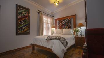 Een slaapkamer met een houten bed, een nachtkastje met een lamp, een rode stoel en een kunstwerk aan de muur.