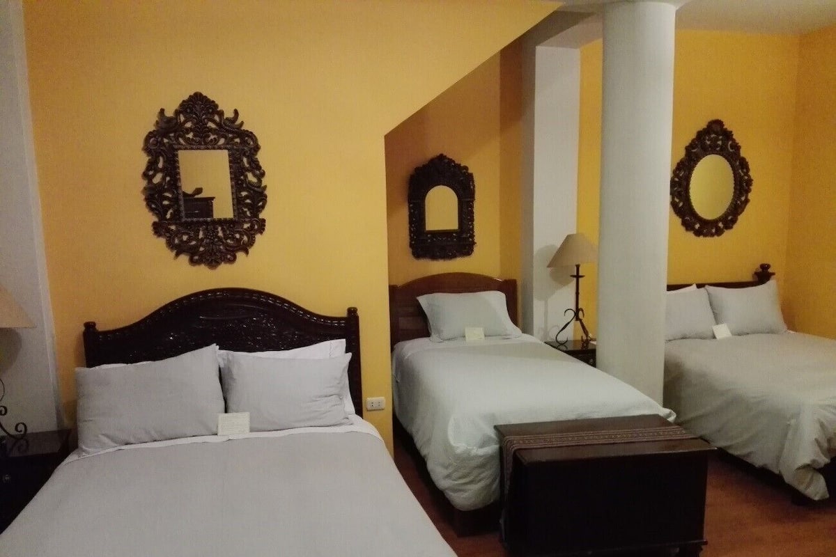 A hotel room with three beds, a wooden headboard, and decorative mirrors on the walls.