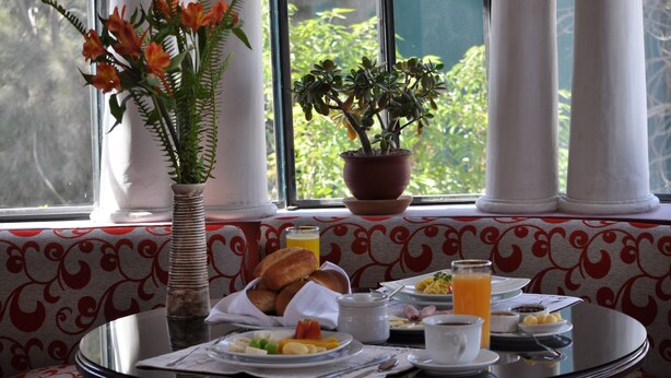 A breakfast table with a variety of dishes, a vase with flowers, and a potted plant by a window with columns. - Casa Arequipa (Arequipa)