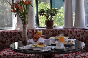 A breakfast table with a variety of dishes, a vase with flowers, and a potted plant by a window with columns. - Casa Arequipa (Arequipa)