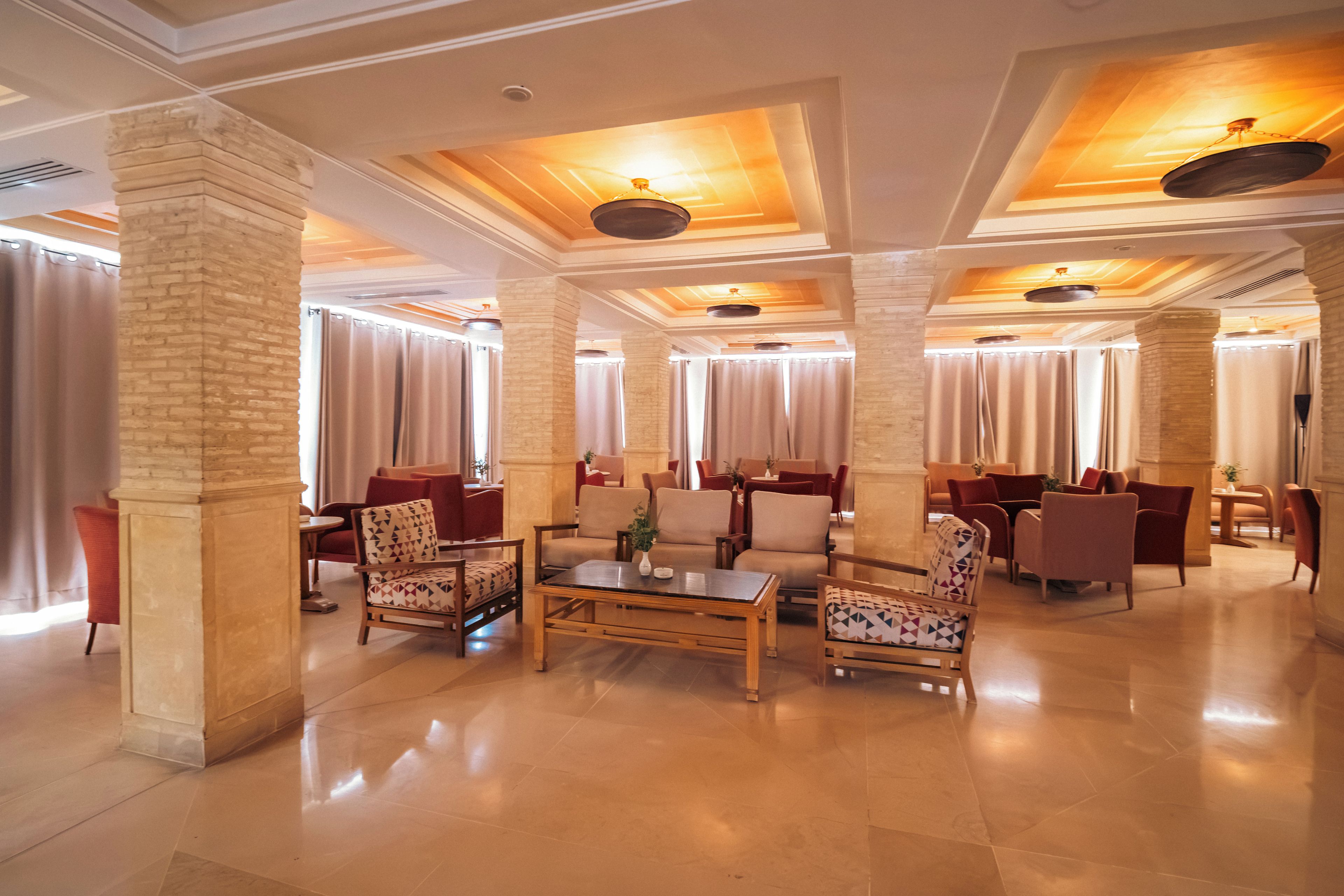 A spacious lobby with a high ceiling, large windows with curtains, and a mix of seating arrangements including sofas and chairs.