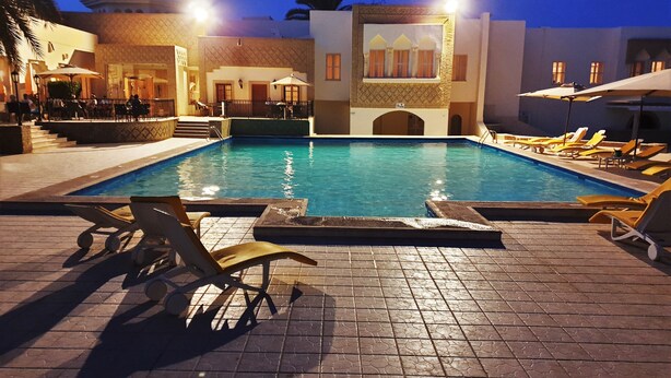 A swimming pool with lounge chairs and a building with a patterned facade.