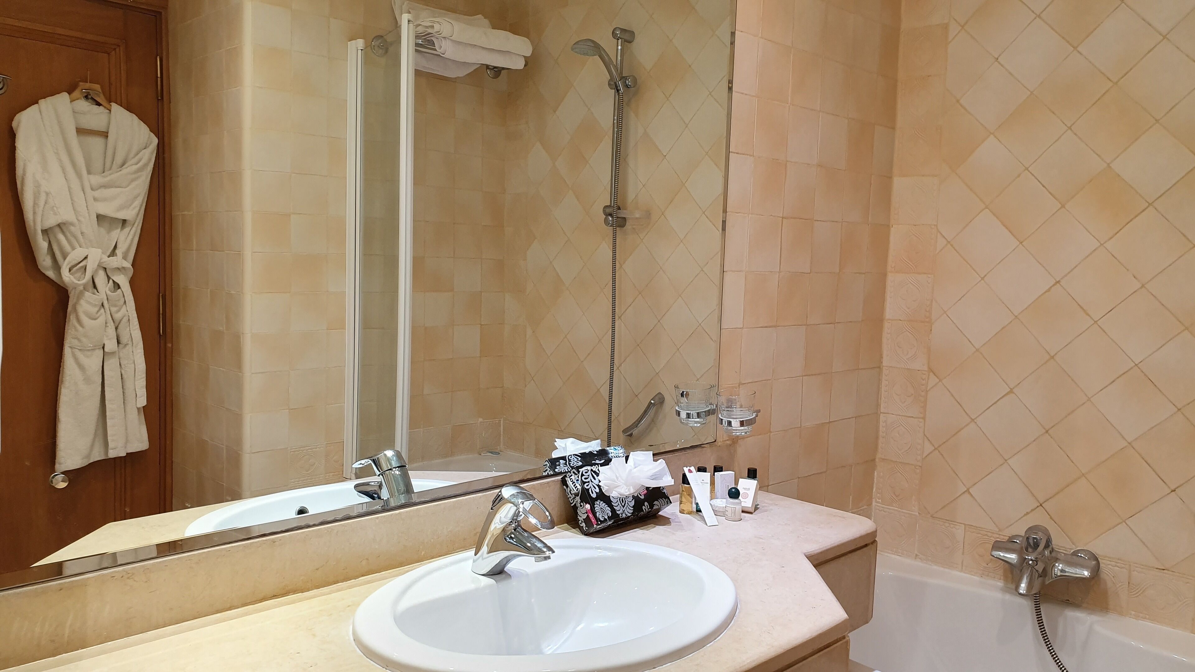 Un baño con lavamanos blanco, un espejo, una ducha y un perchero con bata.