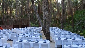 An outdoor dining area with white tablecloths and chairs, surrounded by trees.
