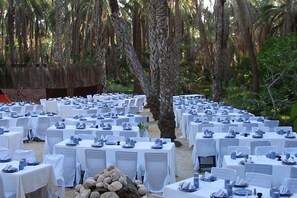 An outdoor dining area with white tablecloths and chairs, surrounded by trees.