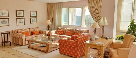 A spacious living room with striped sofas, a glass coffee table, and a red patterned sofa.