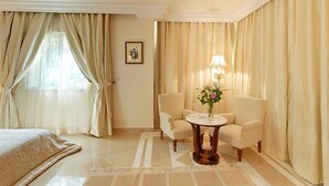 A hotel room with a bed, two armchairs, a small round table with a vase of flowers, and a lamp.