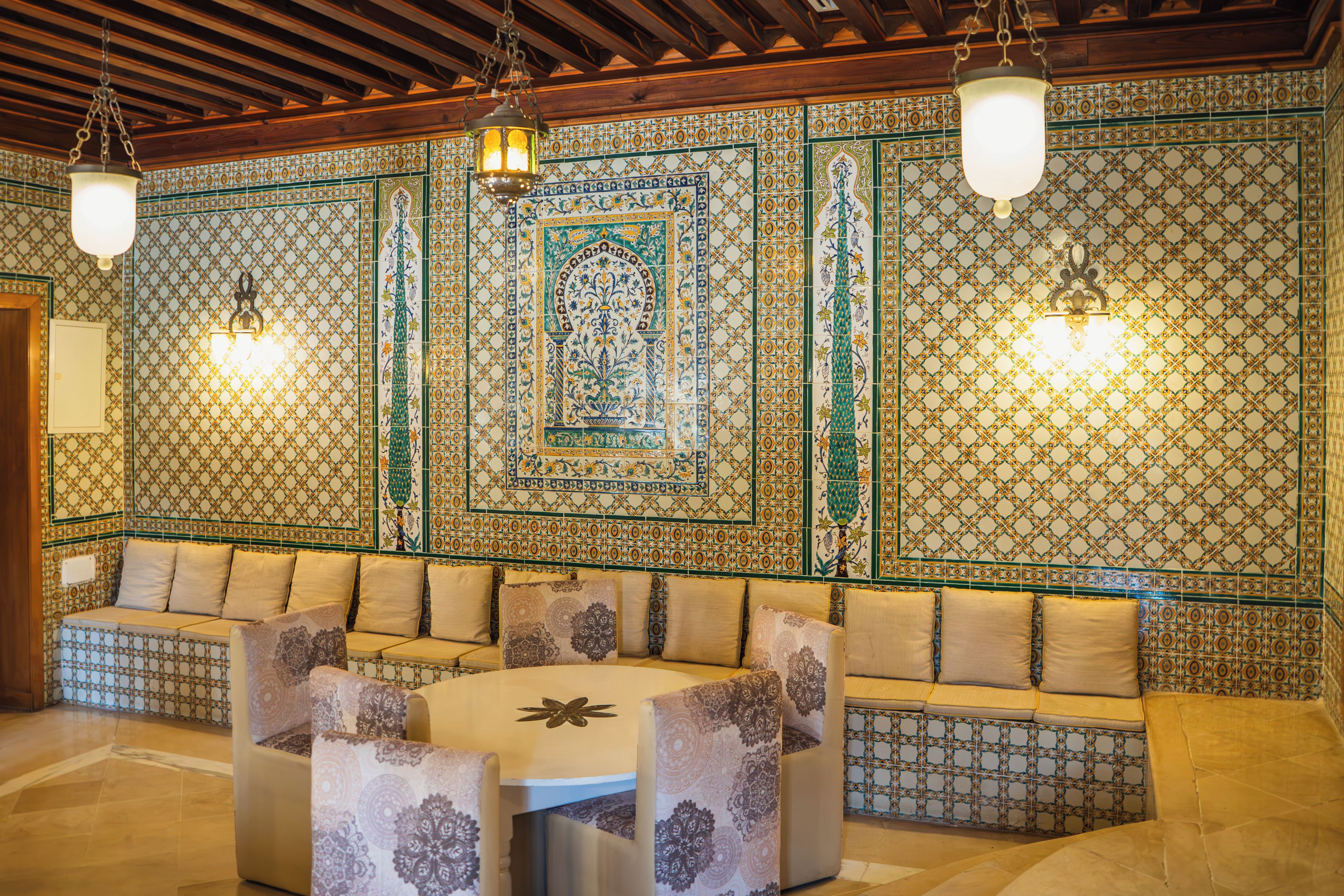 A room with a patterned wall, a sofa with cushions, a table, and hanging lights.