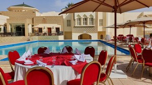 A poolside dining area with tables set for service, red chairs, and umbrellas. - Ras El Ain (Tozeur)