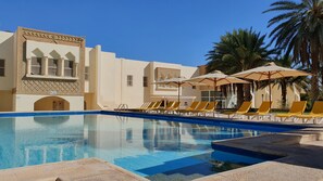 A pool area with sun loungers and umbrellas, surrounded by buildings with traditional architecture. - Ras El Ain (Tozeur)