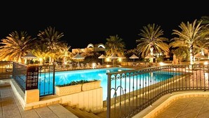 A nighttime pool area with a clear pool, palm trees, and lounge chairs.