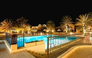 A nighttime pool area with a clear pool, palm trees, and lounge chairs.