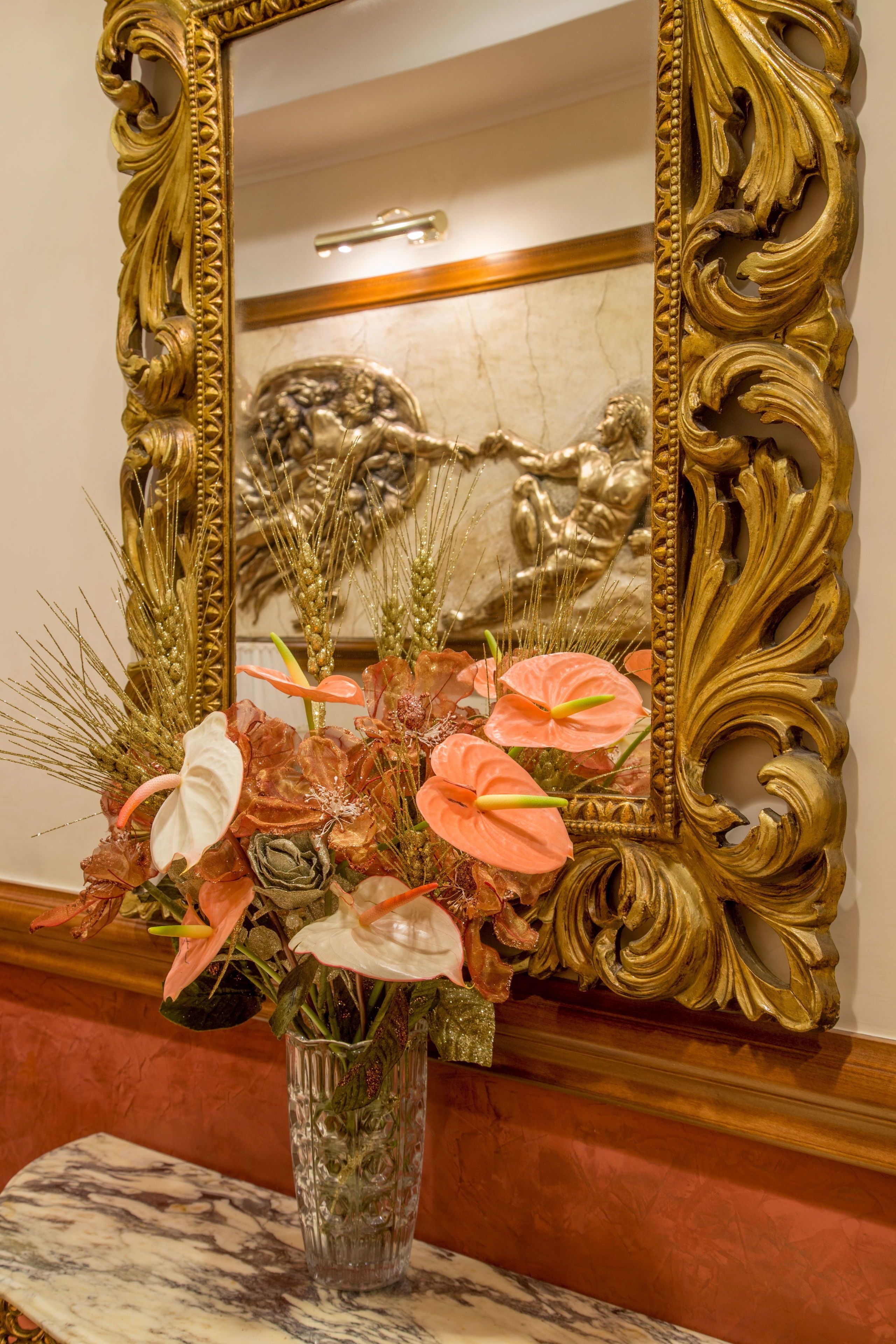 A mirror with an ornate gold frame, a vase with flowers, and a marble table.