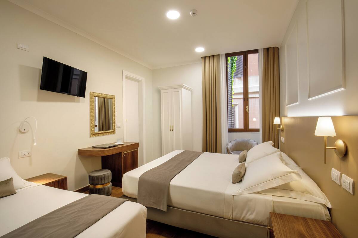 Una camera d'albergo con due letti, televisione, una scrivania e una finestra con tende.