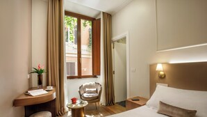A hotel room with a bed, a desk with a chair, a small table, and a window with curtains. - Hotel Forte (Rome)