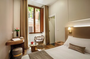 Habitación de hotel con cama, escritorio y silla, una mesita y ventana con cortinas.