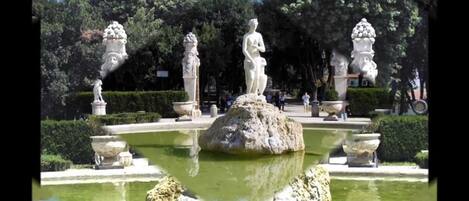 A classical garden with statues and a central fountain.