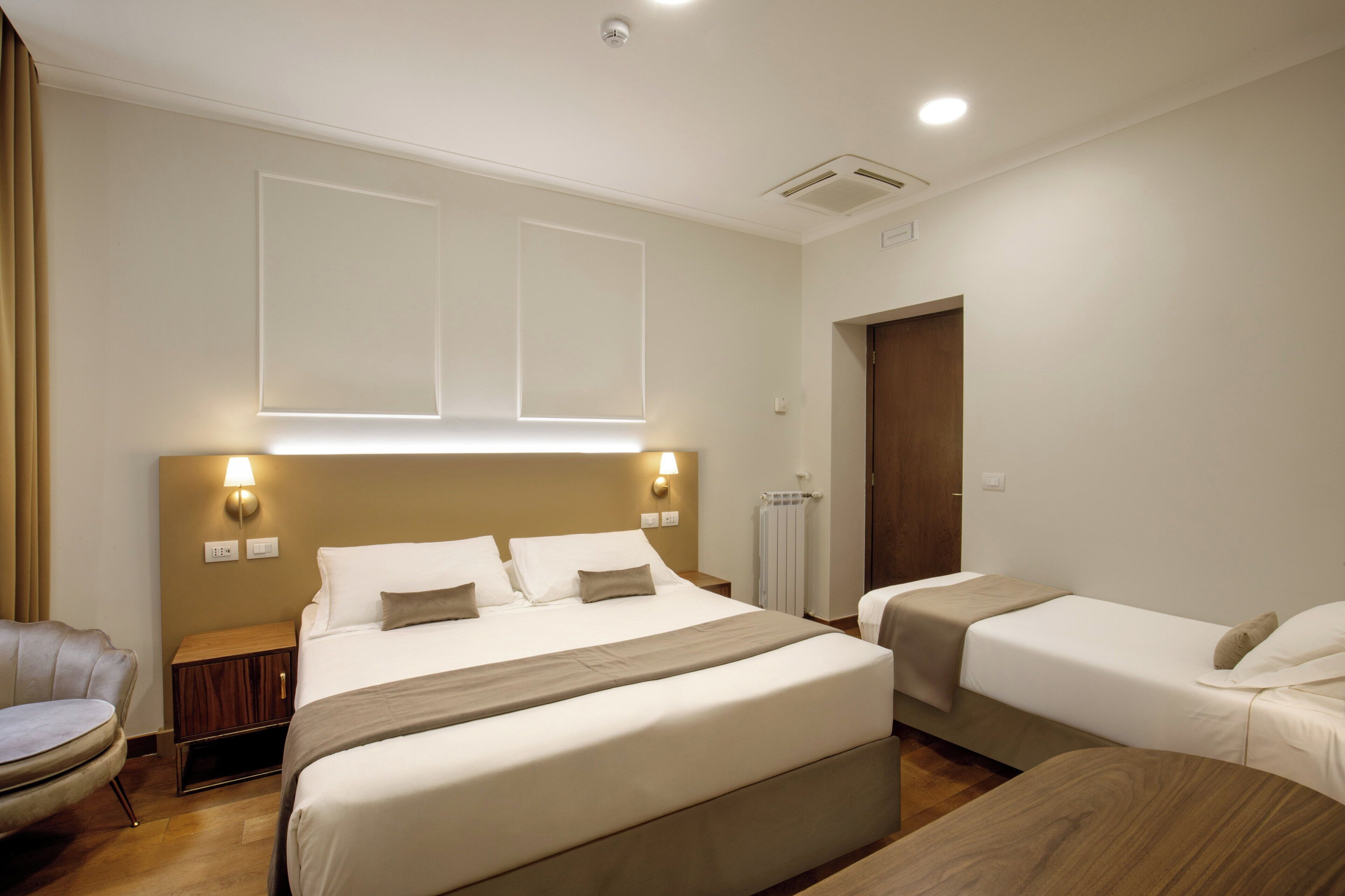 A hotel room with a large bed, two smaller beds, a chair, and a wooden table.
