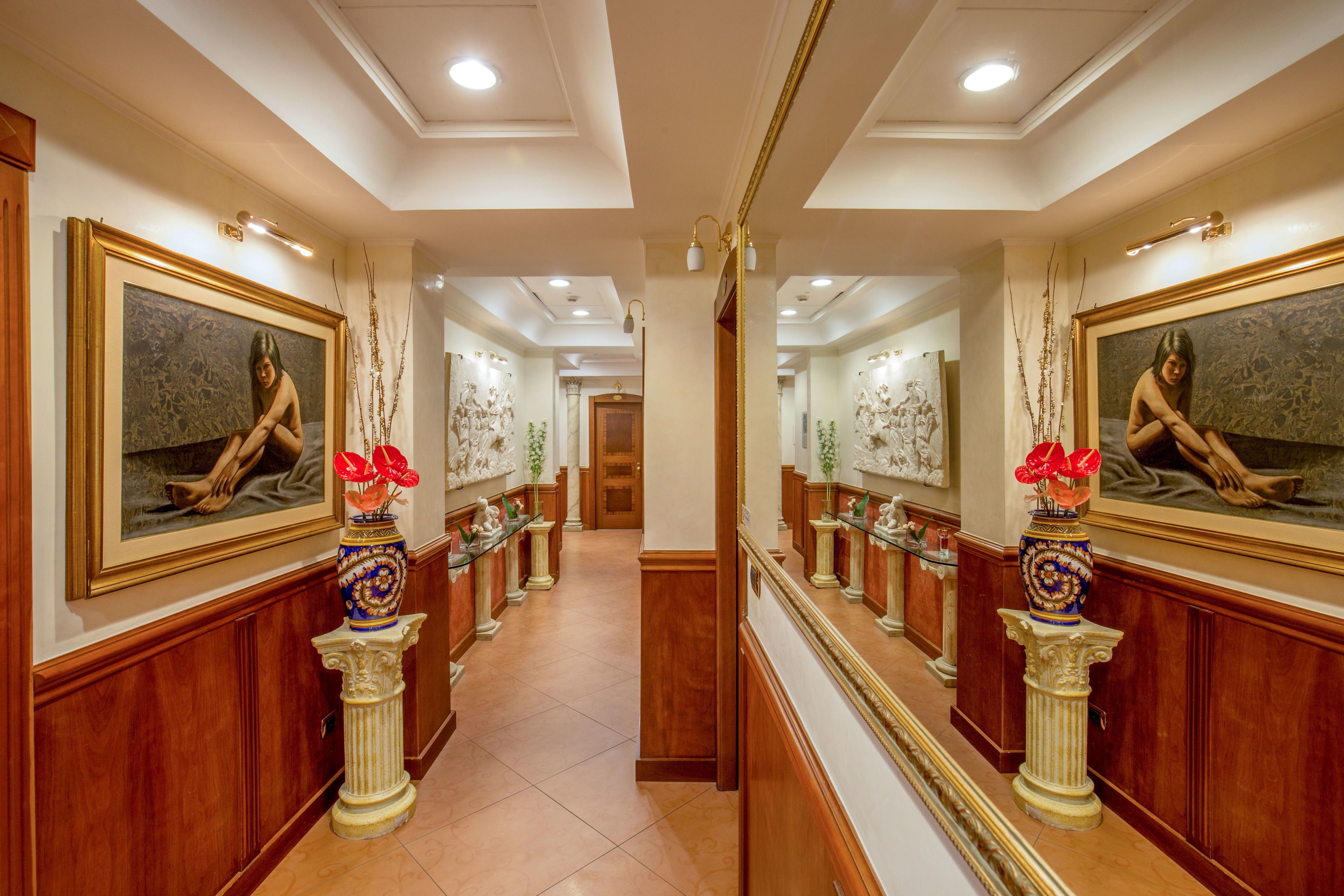 A hallway with mirrored walls, framed artwork, and decorative vases.