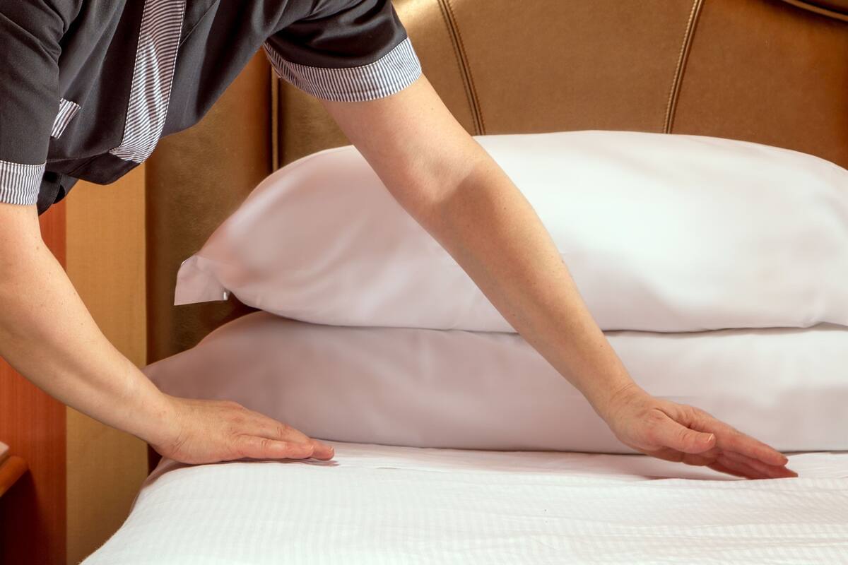 Una mano sistema un cuscino bianco su un letto con testiera.
