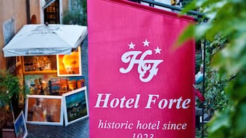 Banner pubblicitario di un hotel storico con la scritta "Hotel Forte" e il testo "albergo storico dal 1923" in una strada cittadina.