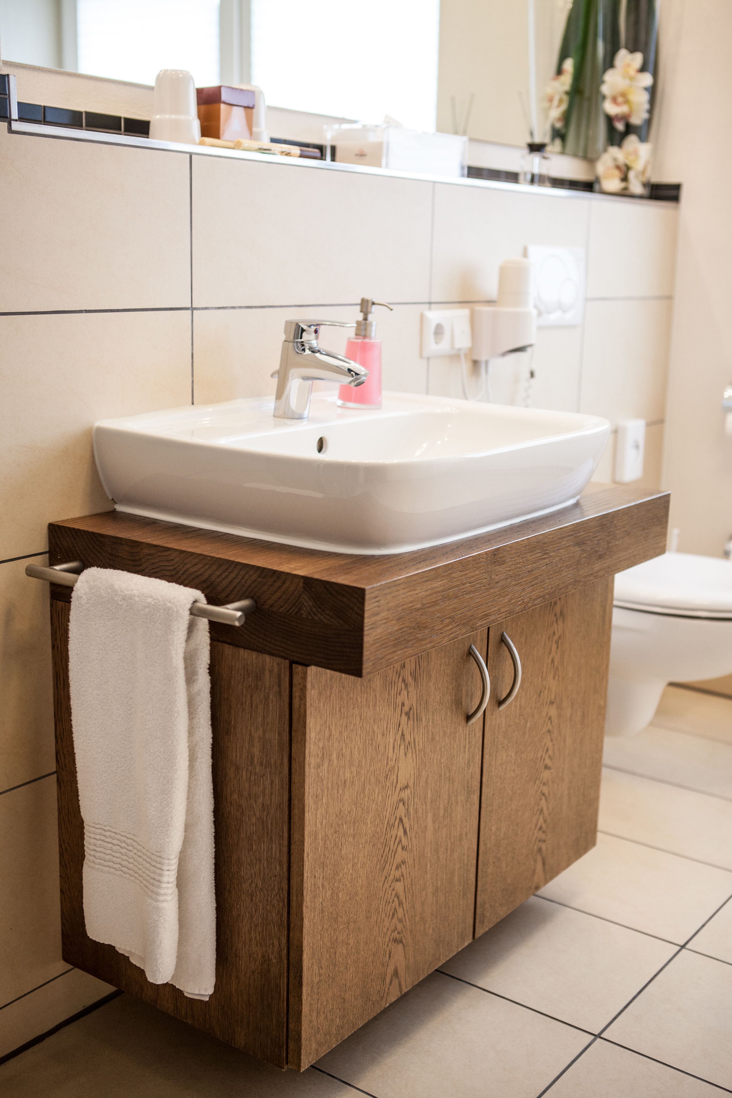 A bathroom with a wooden vanity, a white sink, and a towel hanging on the side.