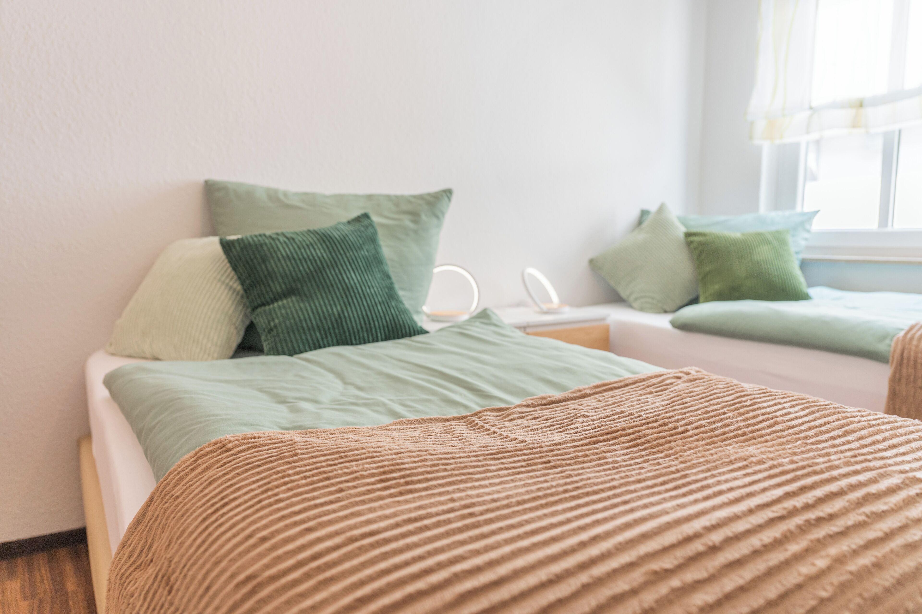 Un dormitorio con cama, almohadas, una mesita de noche y una ventana.