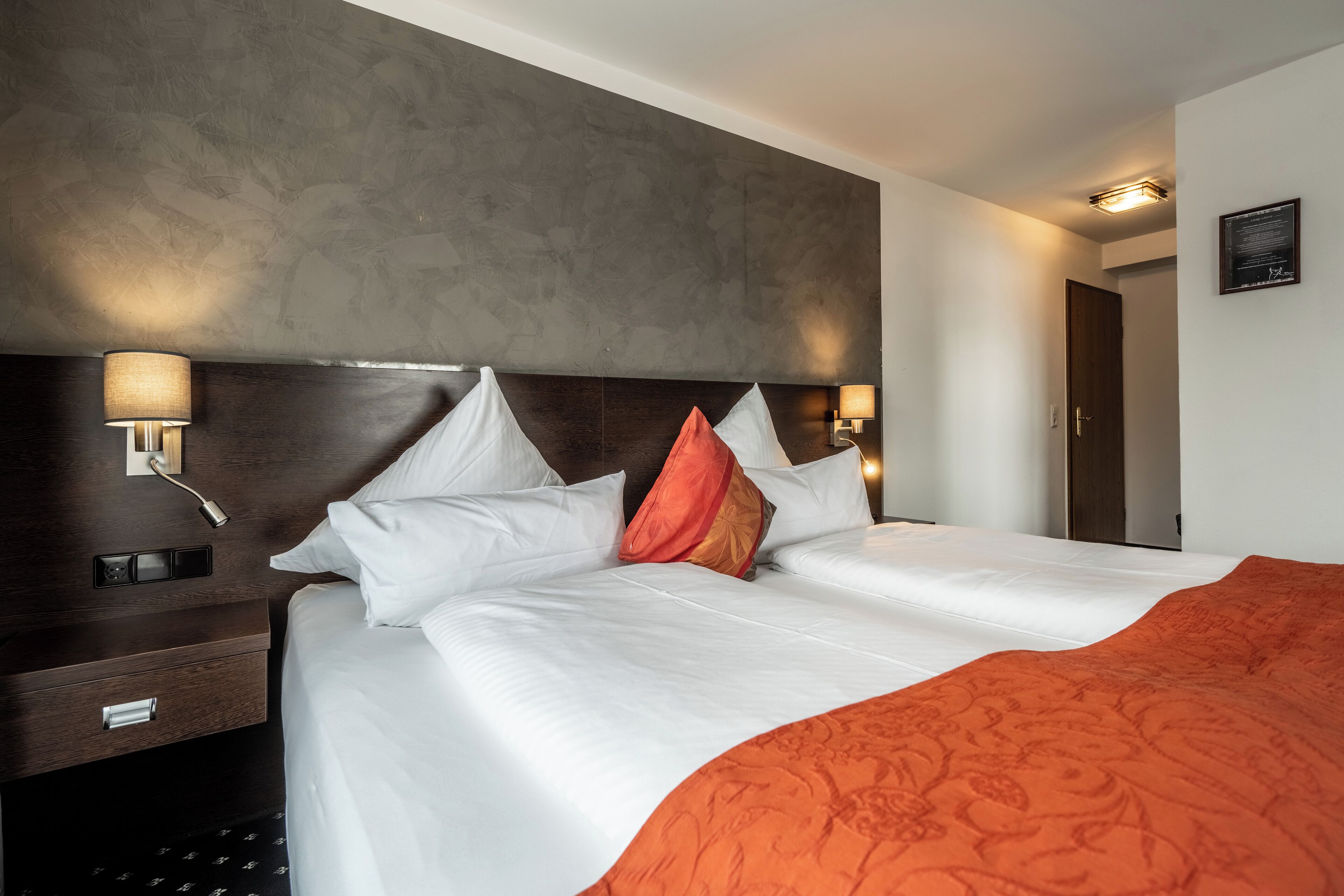 Une chambre d’hôtel avec un grand lit, une tête de lit en bois, des lampes de chevet et un certificat encadré accroché au mur.