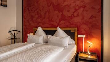 A neatly made bed with white linens and pillows, a bedside lamp, and a red textured wall.