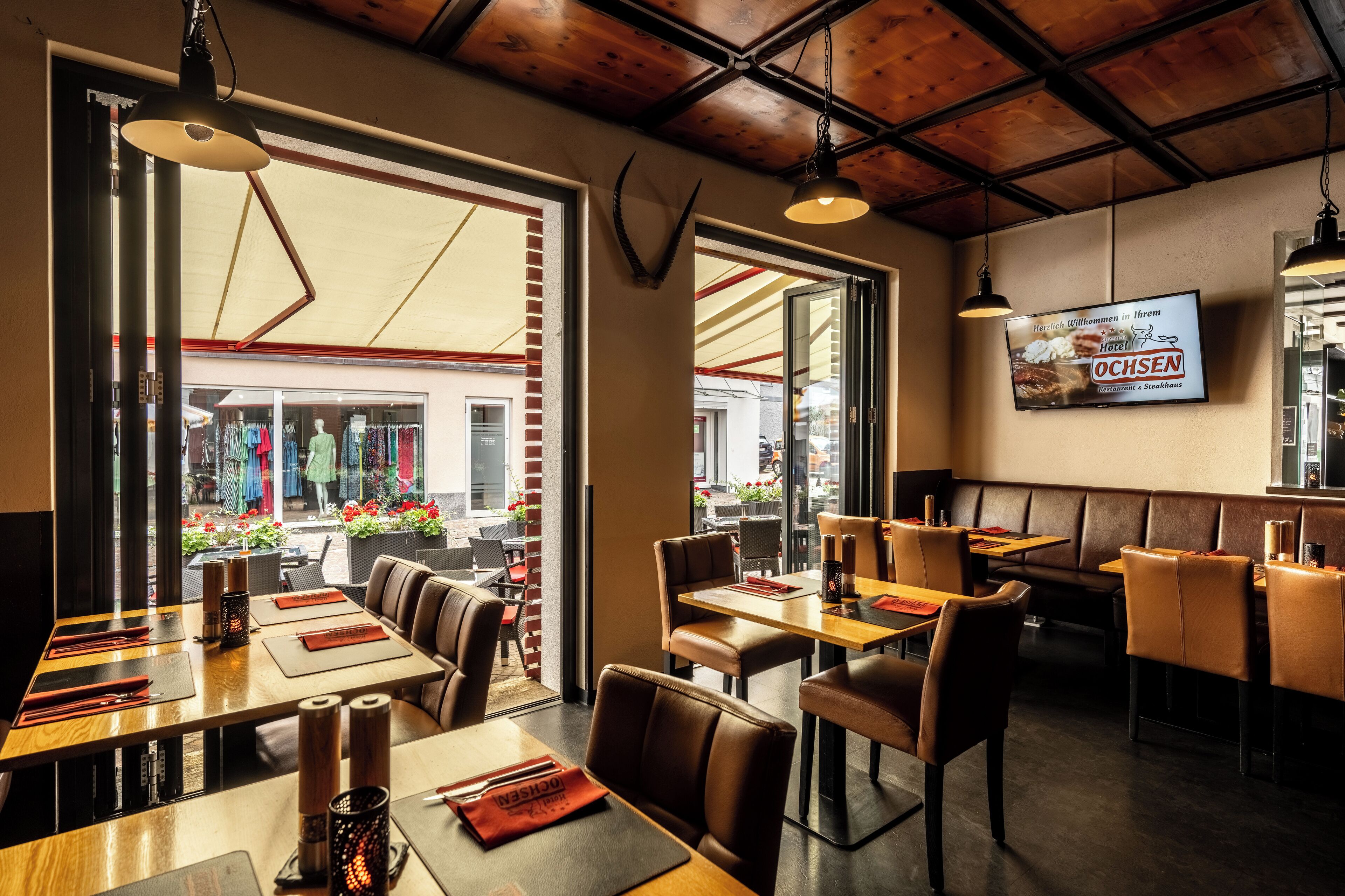 A restaurant with wooden tables and booths, a TV screen on the wall, and large windows overlooking the street.