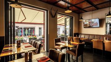 A restaurant with wooden tables and booths, a TV screen on the wall, and large windows overlooking the street.