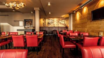 A restaurant with red leather booths and tables, a wooden wall with a mural, and a flat-screen TV mounted on the wall.