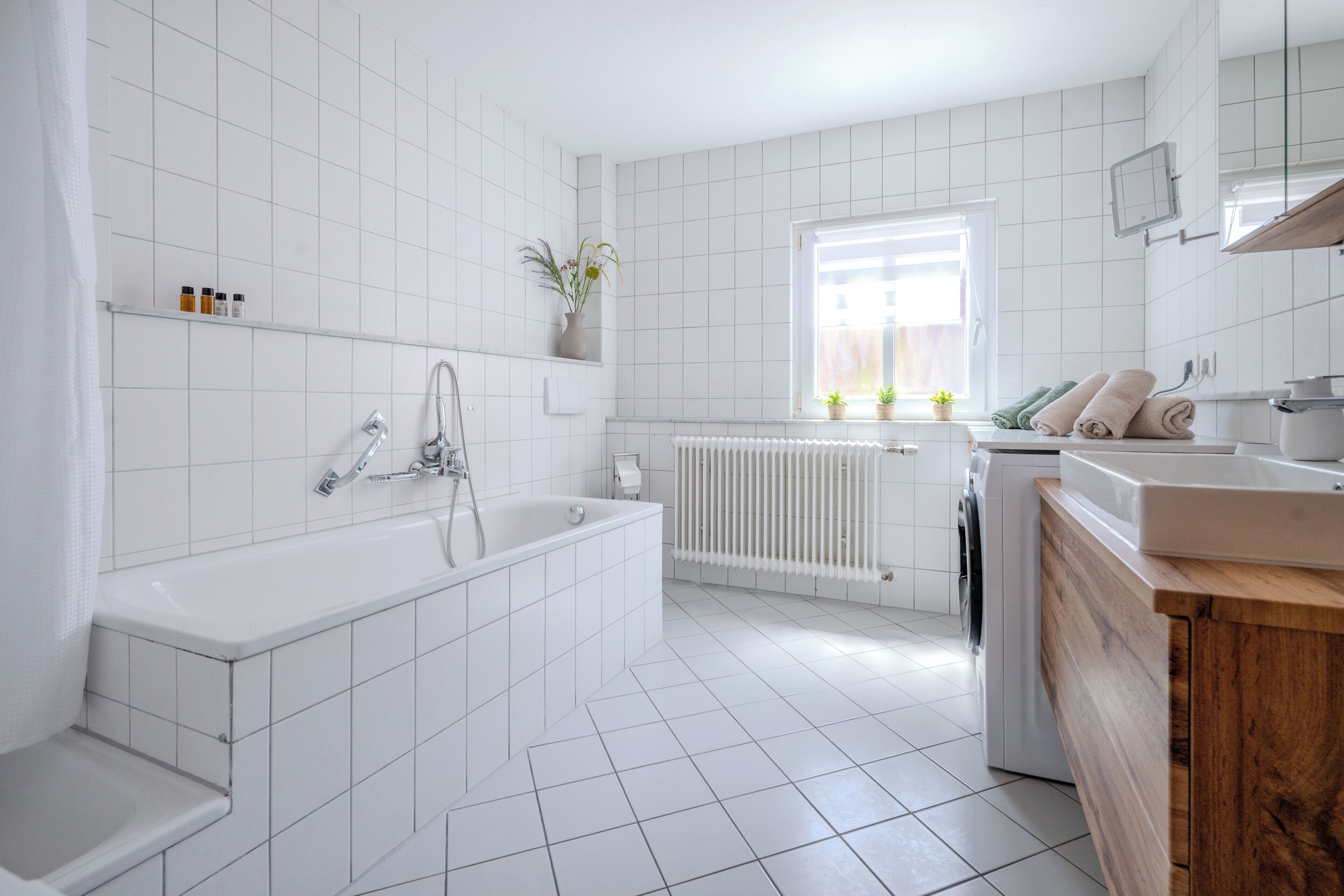 A modern bathroom with a bathtub, a shower, a sink, and a window with plants.