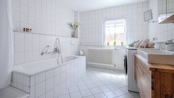 A modern bathroom with a bathtub, a shower, a sink, and a window with plants.