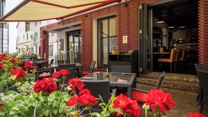 An outdoor cafe with wicker furniture, red flowers, and a red awning. - Hotel Ochsen (Bad Saulgau)
