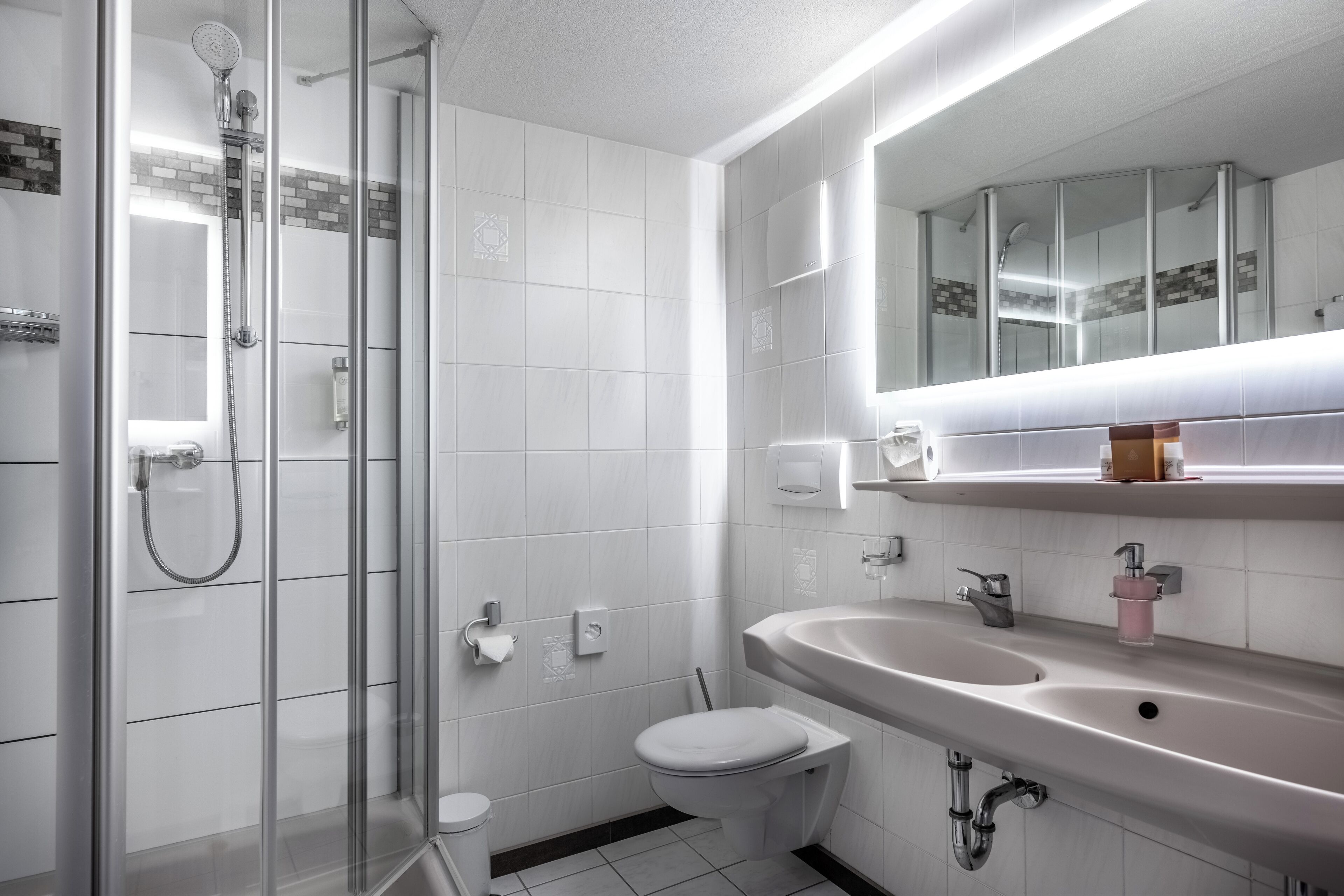 Un baño moderno con ducha de vidrio, inodoro blanco y un lavabo grande con espejo arriba.