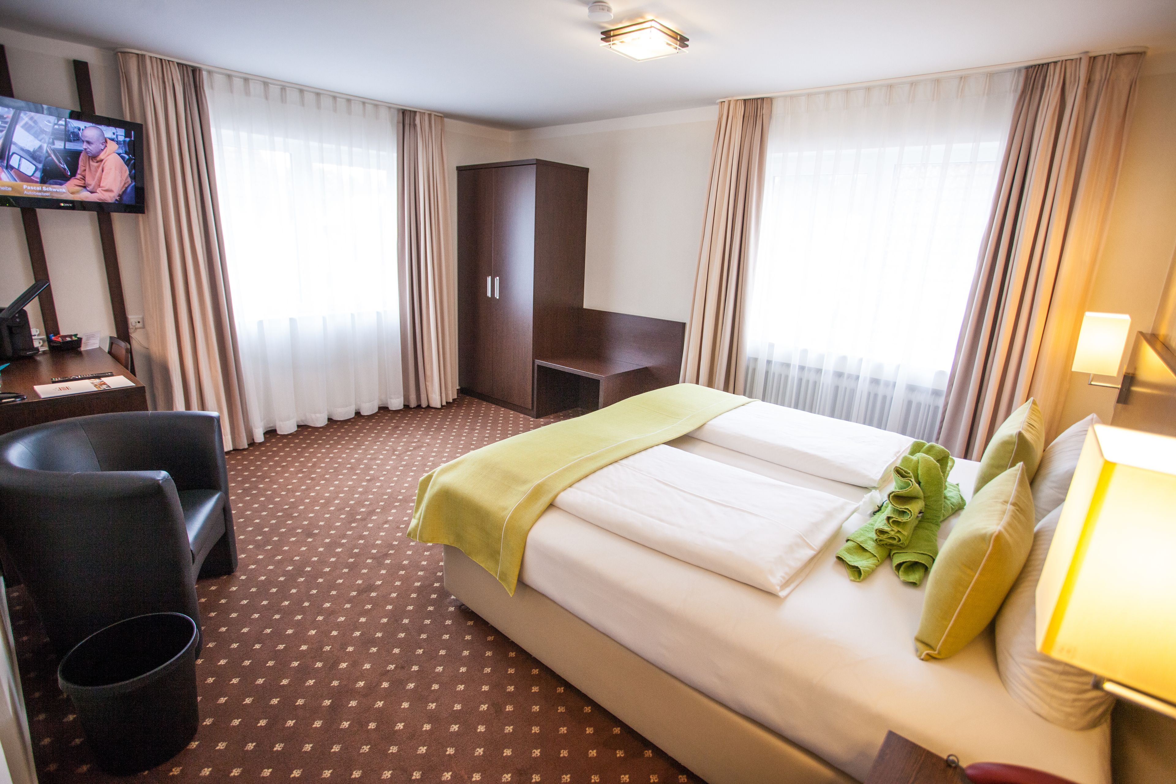 A hotel room with a bed, a desk with a chair, a television, and a wardrobe.