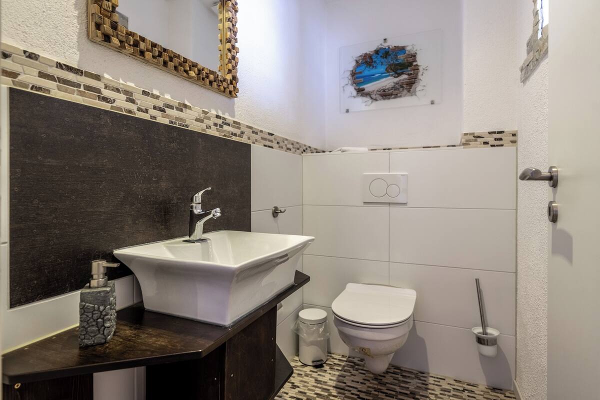 A bathroom with a large white sink, dark countertop, and a tiled floor.