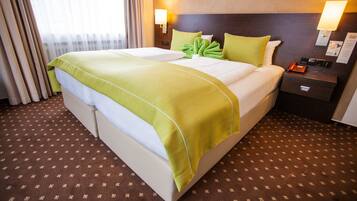 Una habitación de hotel con una cama grande, almohadas verdes, una mesita de noche con teléfono y una lámpara de pared.