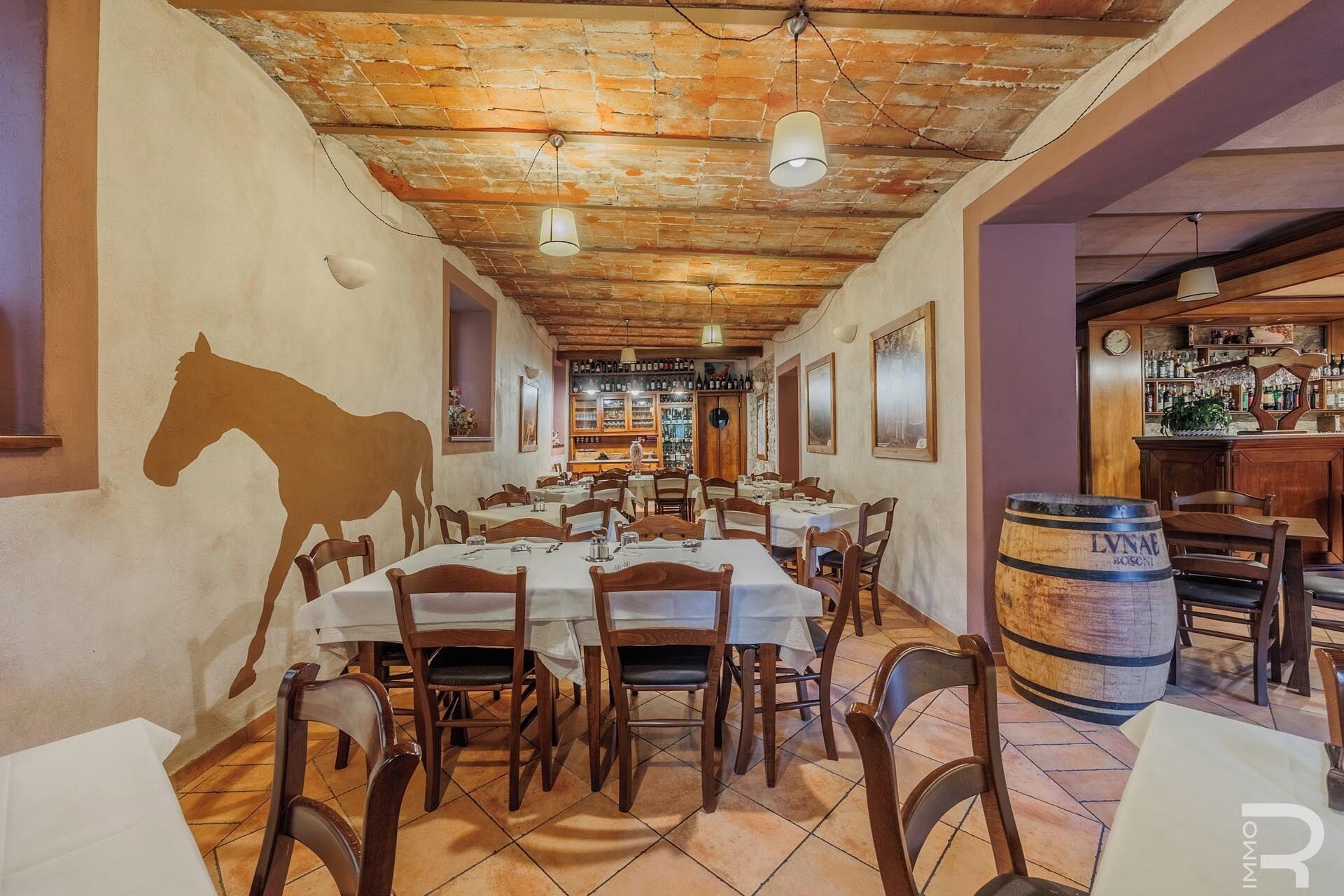 A restaurant with wooden tables and chairs, a brick ceiling, and a bar area with bottles and glasses.