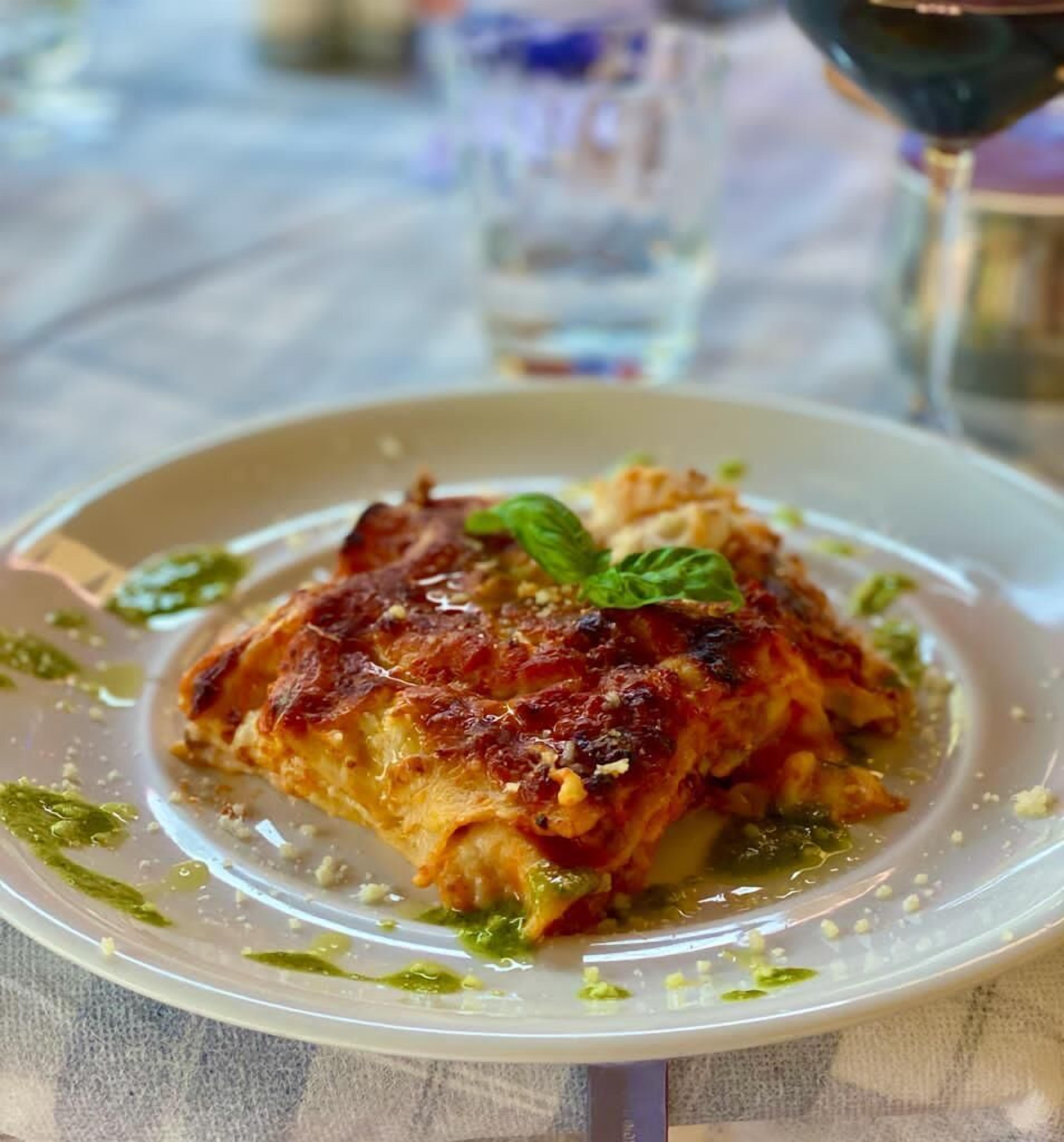 Un plato de comida con una costra dorado-marrón, adornado con una hoja de menta y rodeado de salsa verde y migas.