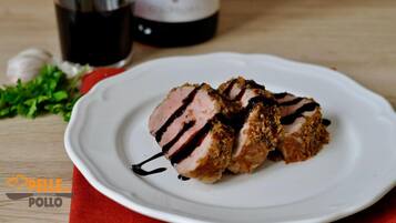 Un plato de carne en rodajas con salsa oscura, una botella de vino tinto, y ajo y hierbas sobre una mesa de madera.