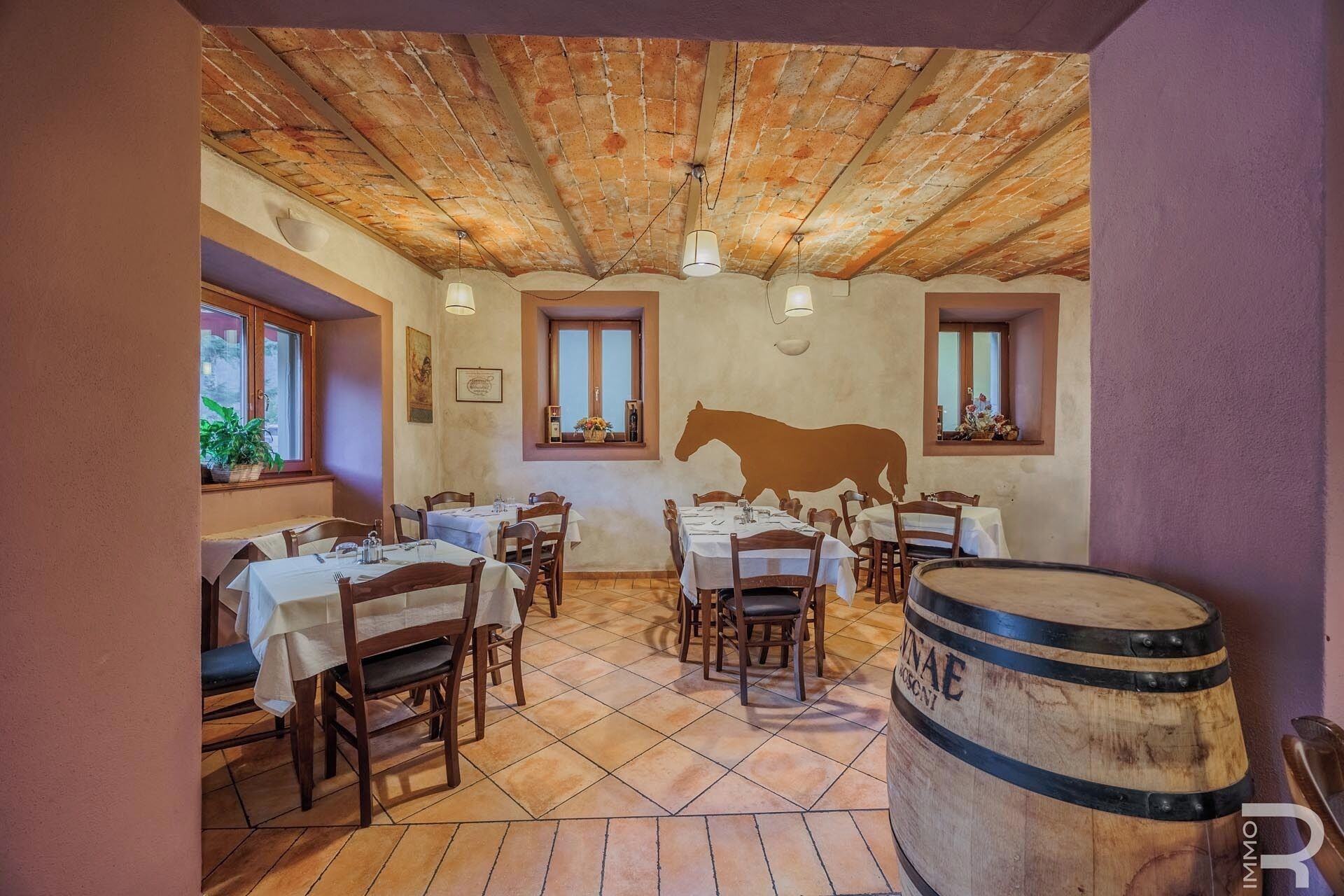 A rustic dining area with wooden tables and chairs, a brick ceiling, and a barrel in the foreground.