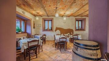 A rustic dining area with wooden tables and chairs, a brick ceiling, and a barrel in the foreground.