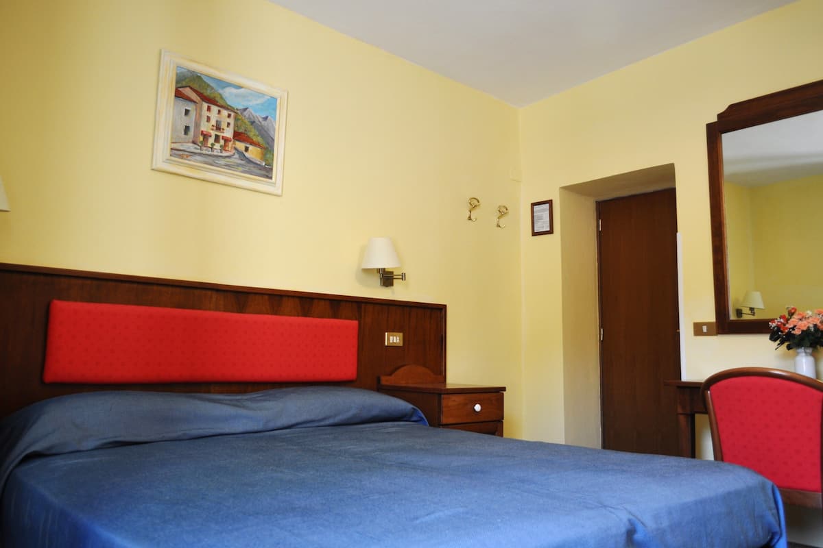 Ein Hotelzimmer mit einem Bett, einem Nachttisch, einem Sessel, einem Spiegel und einem Bild an der Wand.