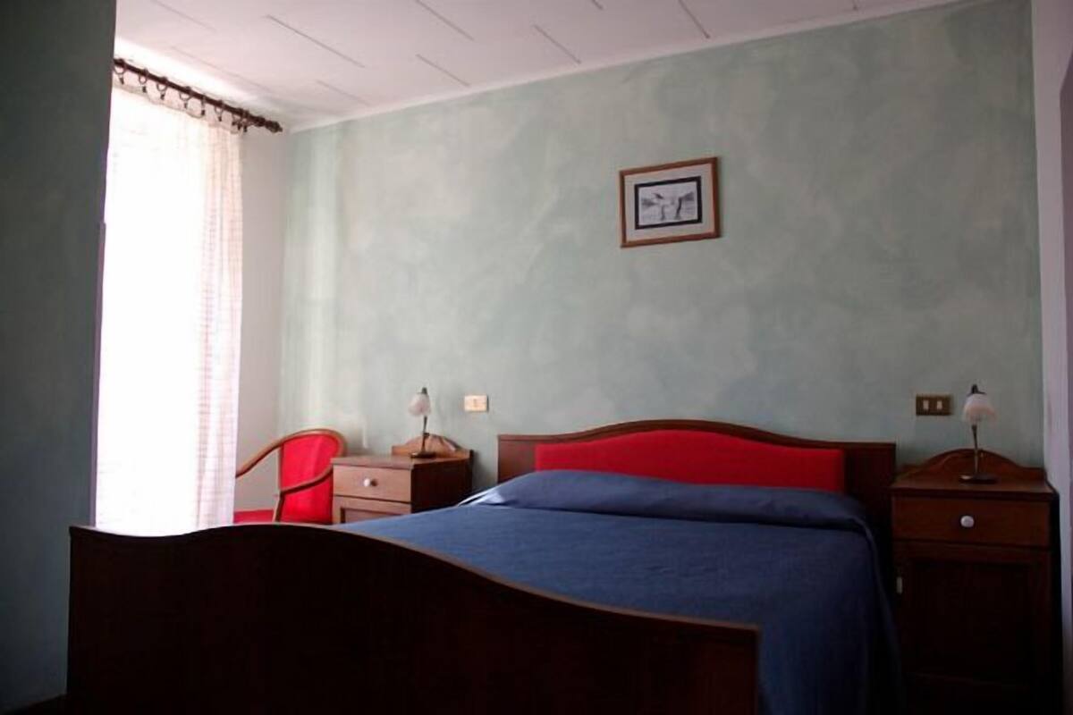 Ein Schlafzimmer mit einem Bett, einem Nachttisch, einem Sessel und einem Fenster mit Vorhängen.